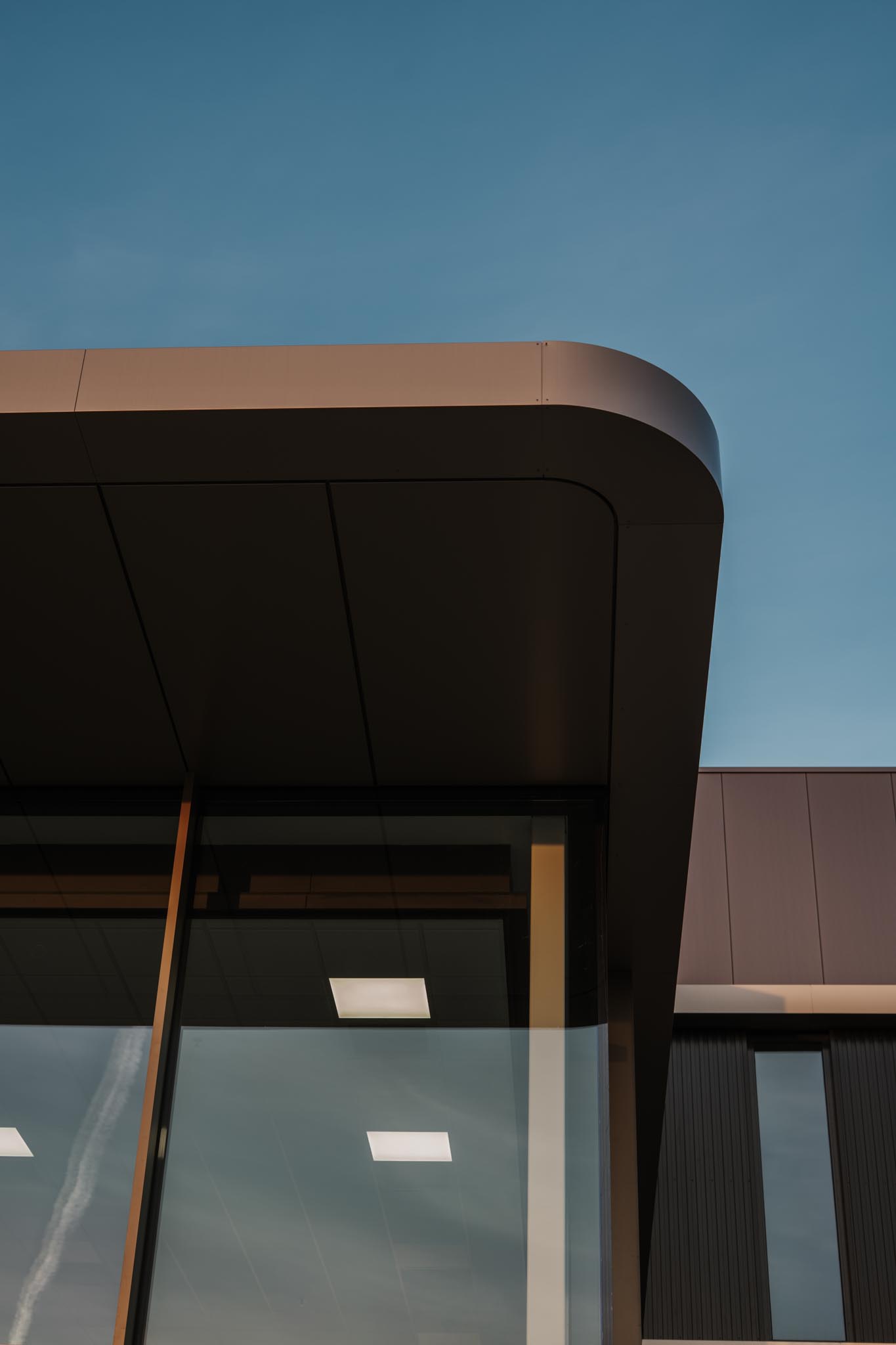 Modern building façade with large glass windows reflecting a blue sky at sunset.
