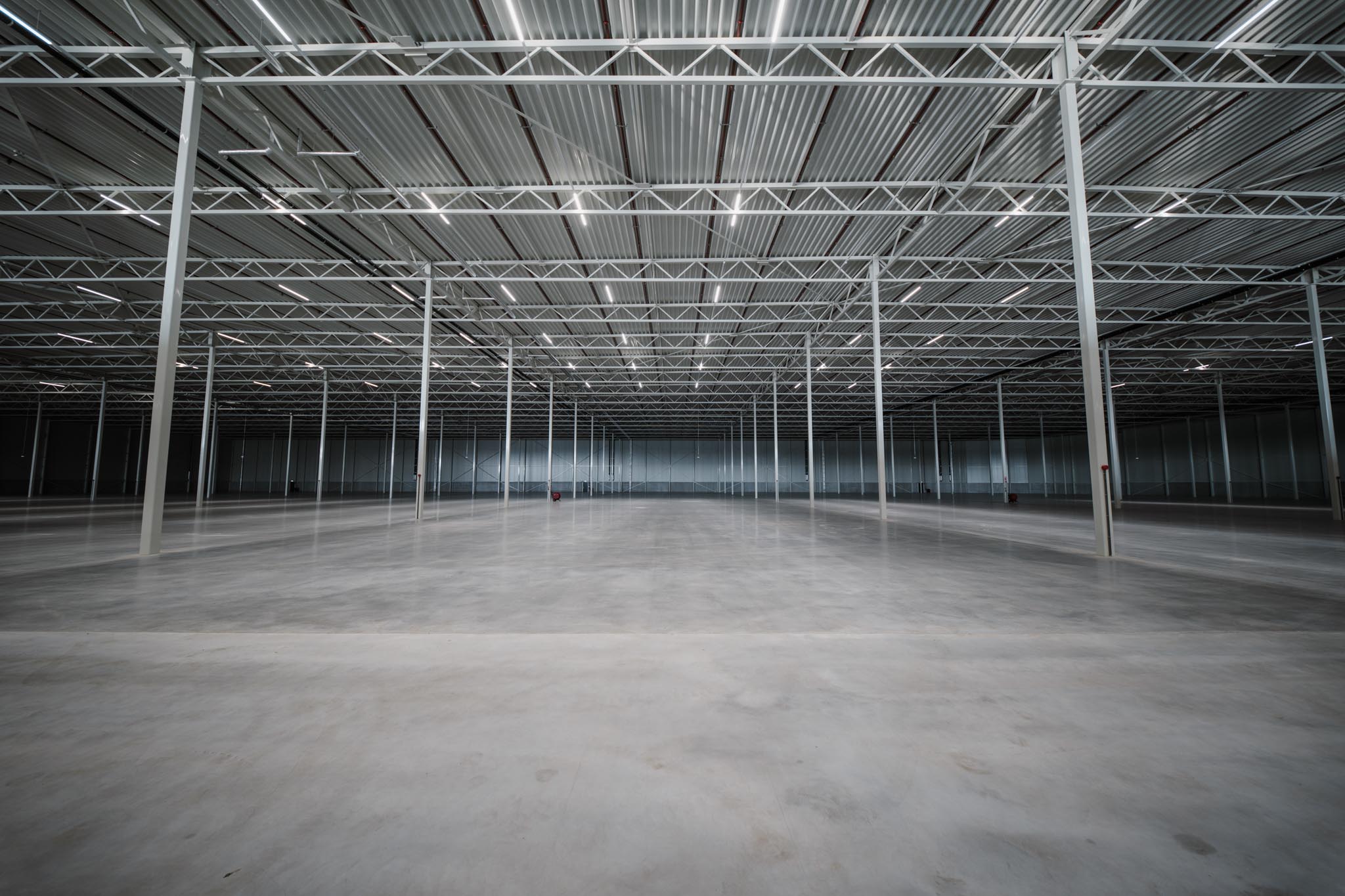 Spacious empty industrial warehouse interior with concrete floor and metal support beams.