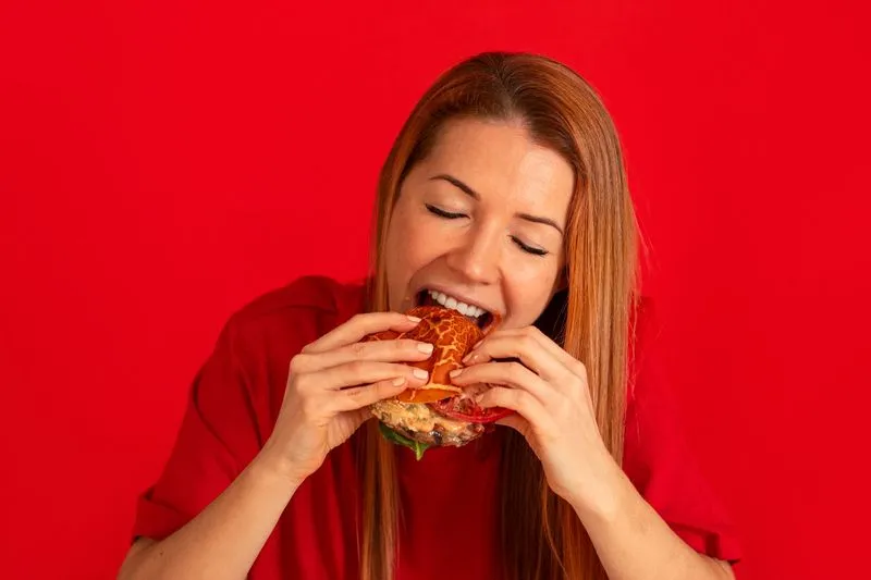 A woman in a red shirt is eating a sandwich.
