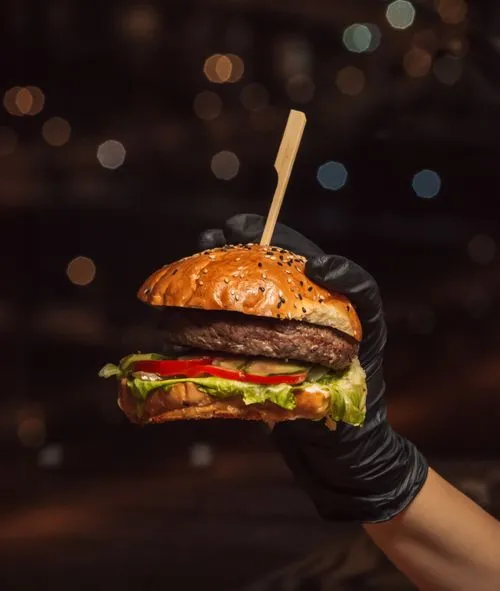 A hand holding a hamburger with a toothpick in it.