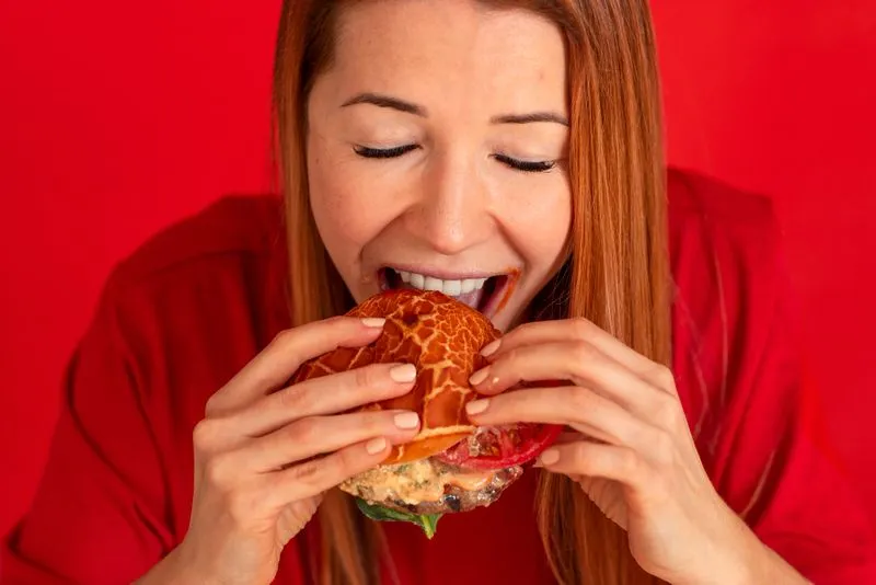 A woman in a red shirt is eating a sandwich.