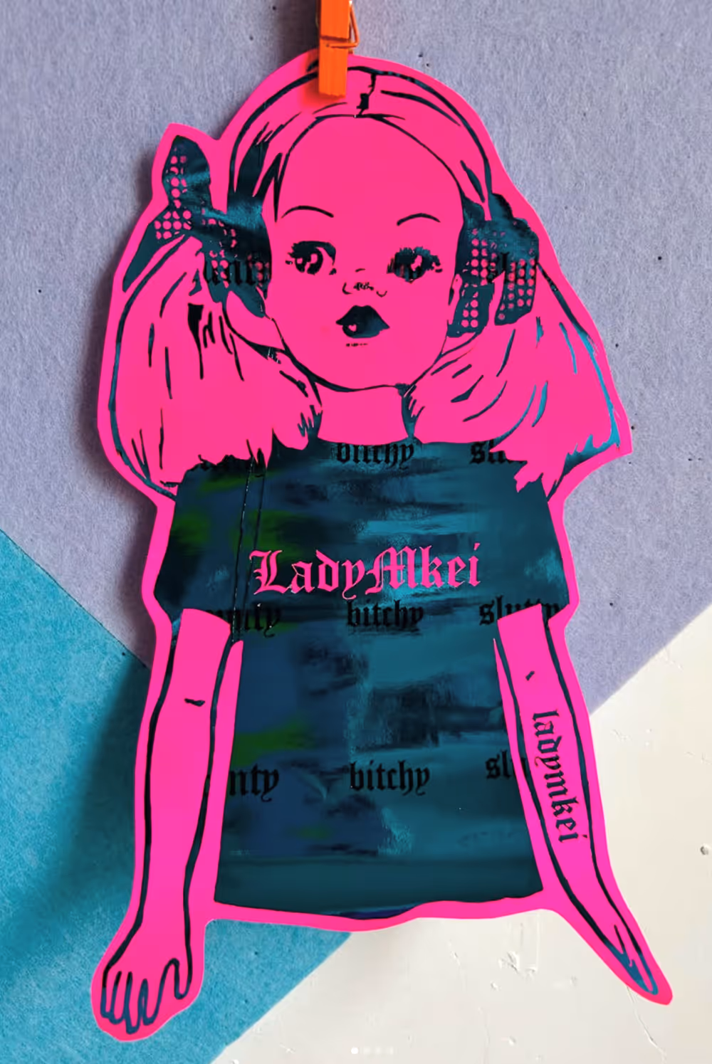 Bright pink cartoon girl with bows and a blue shirt reading LadyMkei pinned to a wall.