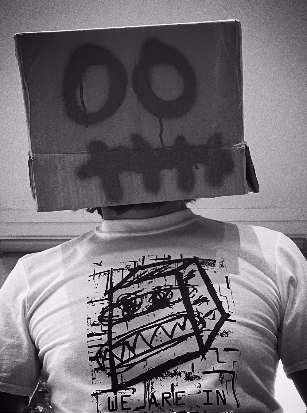 Person wearing a cardboard box mask with eyes and teeth drawn, and a shirt with a similar face illustration.