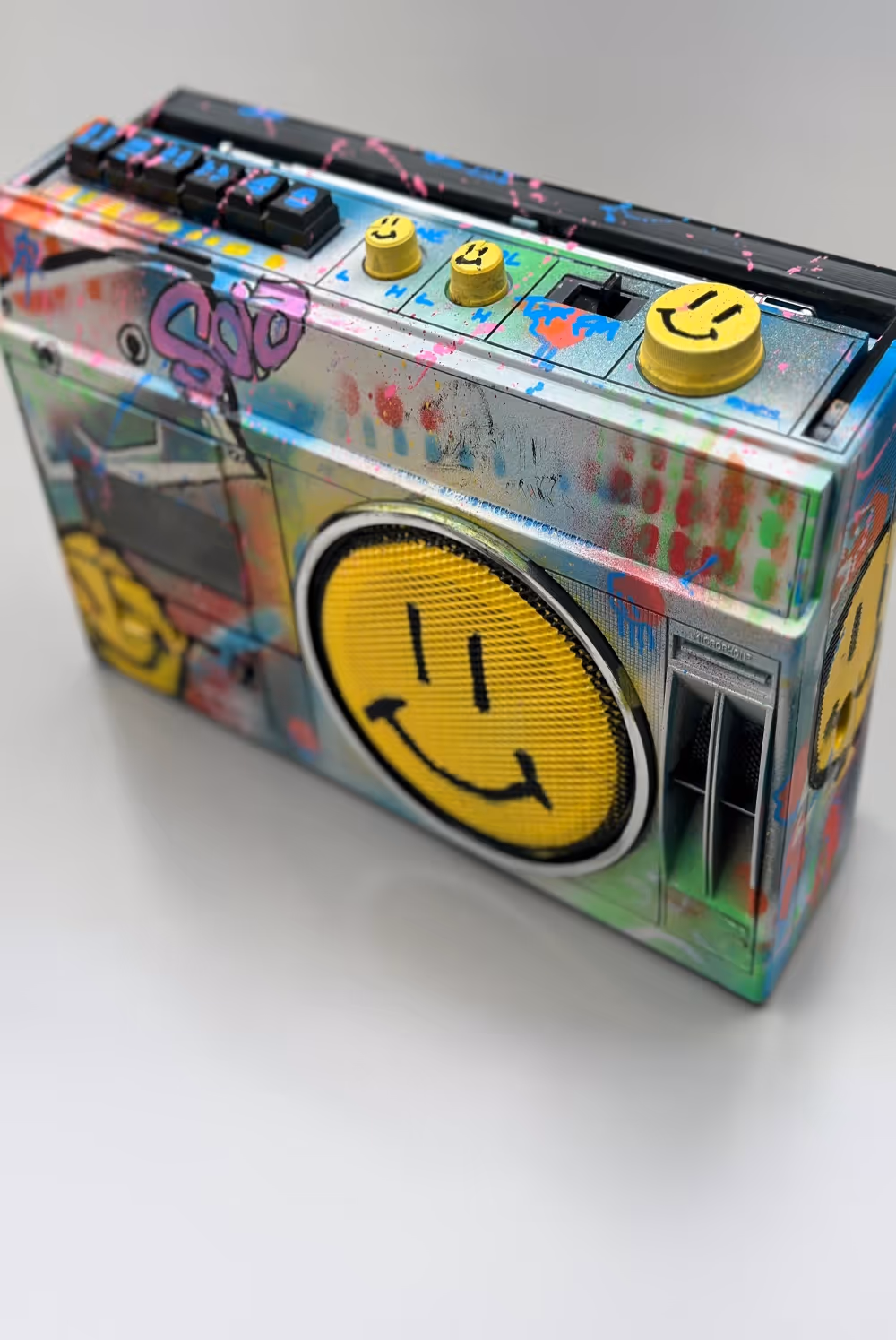 Colorfully graffiti-painted retro boombox with yellow smiley faces on speaker and knobs.