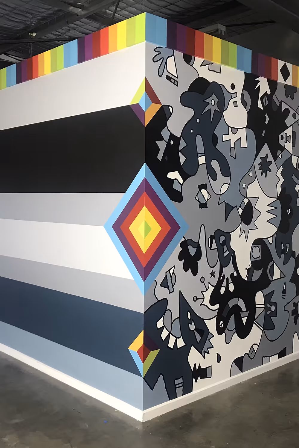 Corner wall with black, gray abstract art on one side and horizontal stripes with a rainbow border on top.