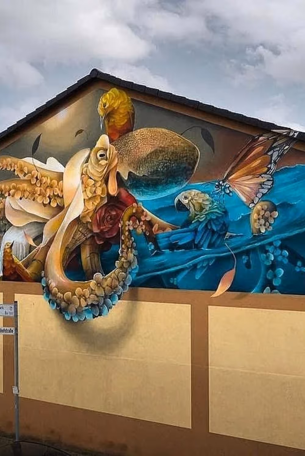 Colorful mural of sea creatures like octopus and birds blending with butterfly wings on building wall.