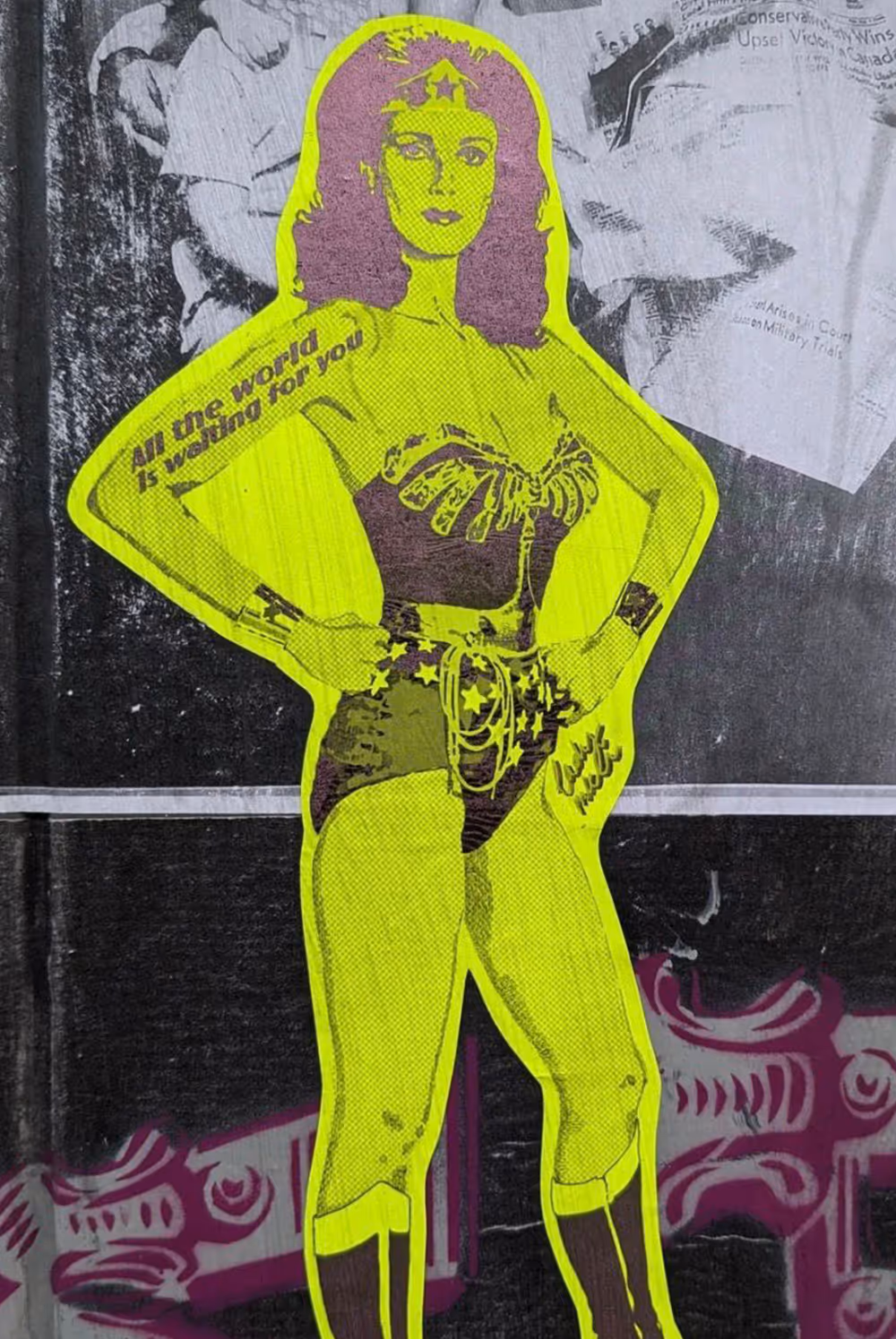 Street art of Wonder Woman in neon yellow with text 'All the world is waiting for you' on arm.