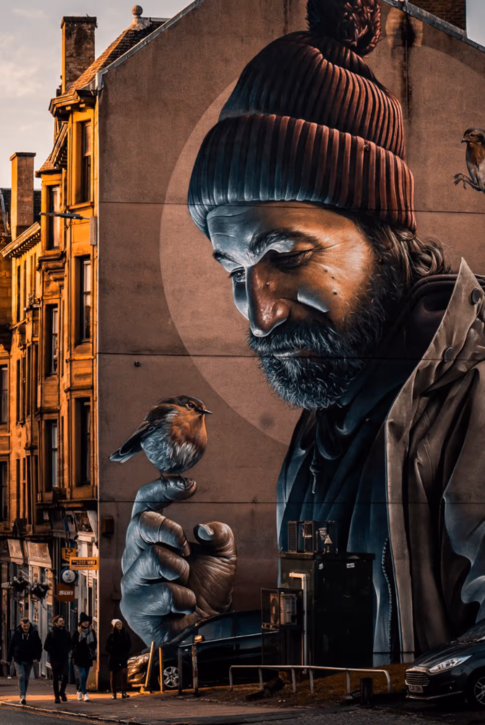 Large street mural of a man with a beanie gently holding a small bird on his finger.