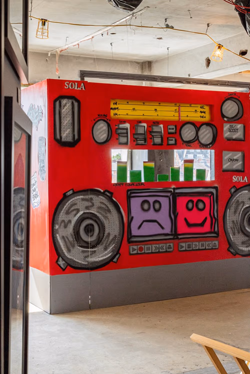 Large red graffiti artwork of a boombox with sad and happy faces on cassette tapes indoors.