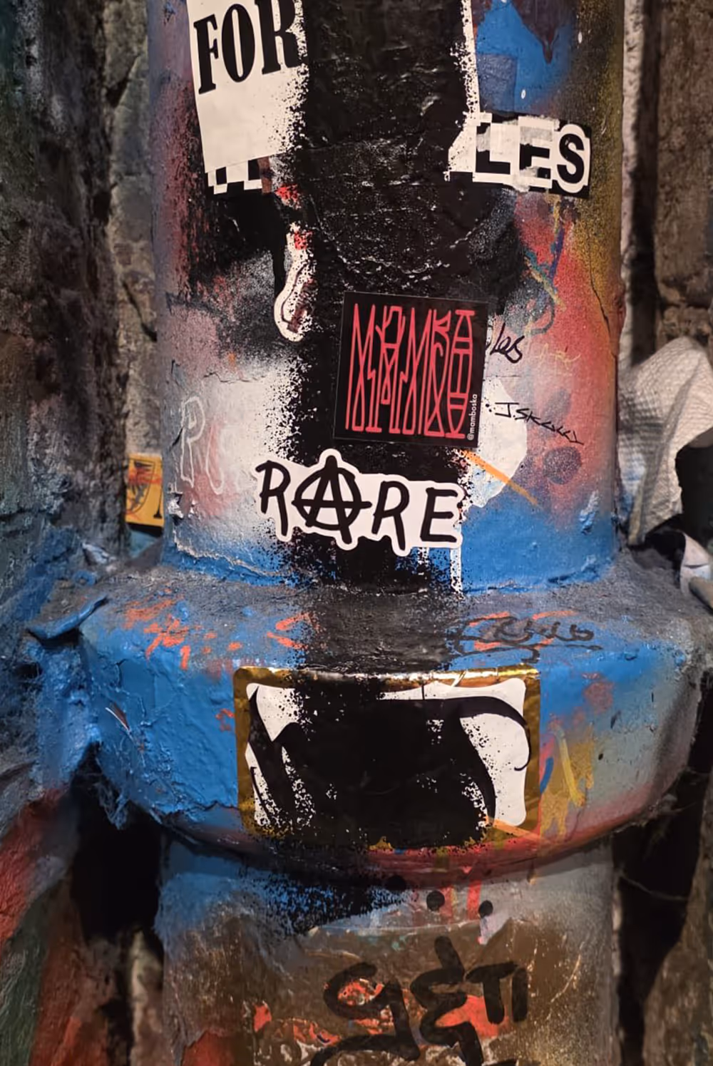 Graffiti-covered cylindrical surface with stickers, including one saying 'RARE' with an anarchy symbol.