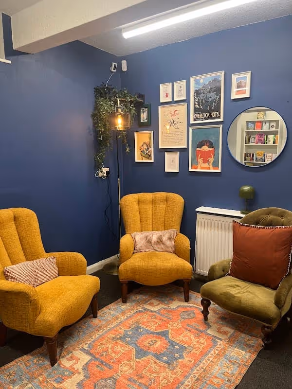 Cozy reading corner with mustard and olive armchairs, patterned rug, wall art, and blue walls.