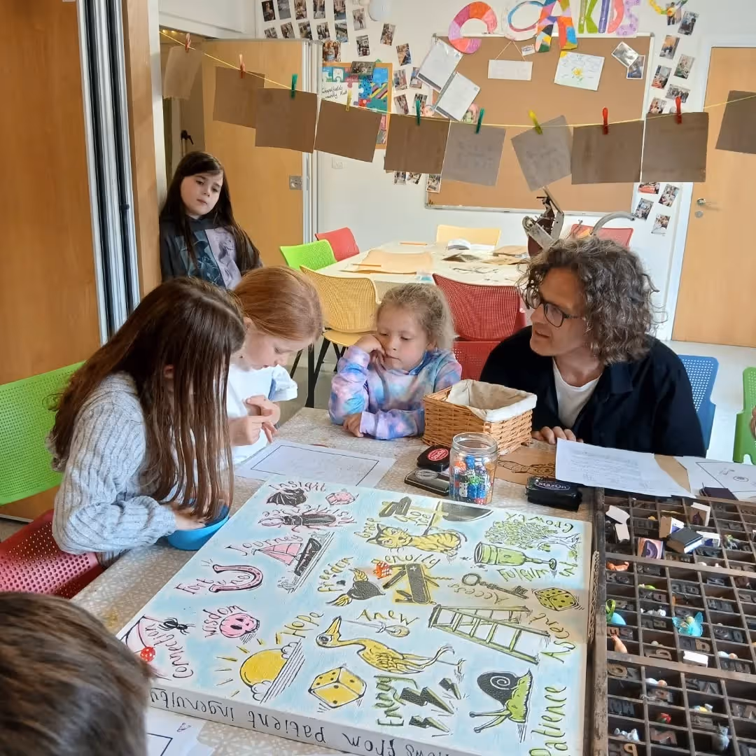 Children and an adult engaged in a creative learning activity with illustrated cards on a table.