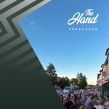 Crowd gathered outside on a street near shops under a clear blue sky at The Hand Freehouse.