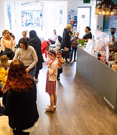 People socializing and a girl dressed as a fairy standing in a bright cafe with a counter and menu board.