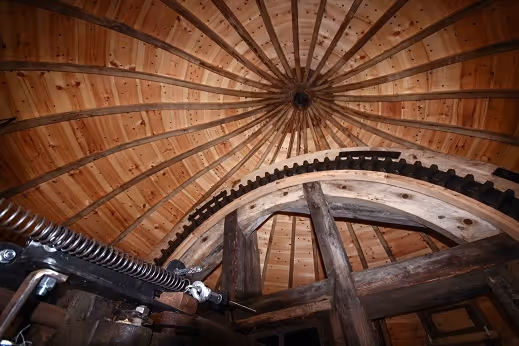 Interior view of a wooden dome ceiling with radial beams and mechanical gears beneath it.