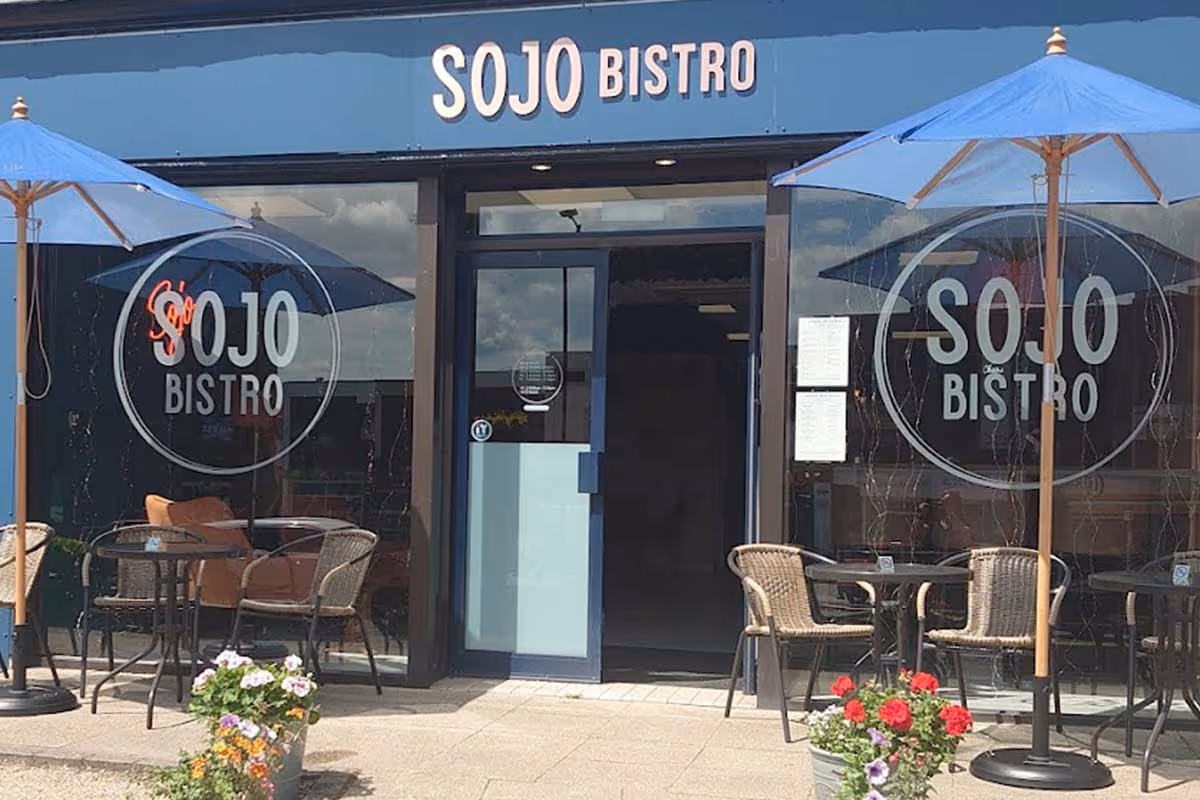 Outdoor seating with blue umbrellas and wicker chairs at Sojo Bistro with glass doors and windows.