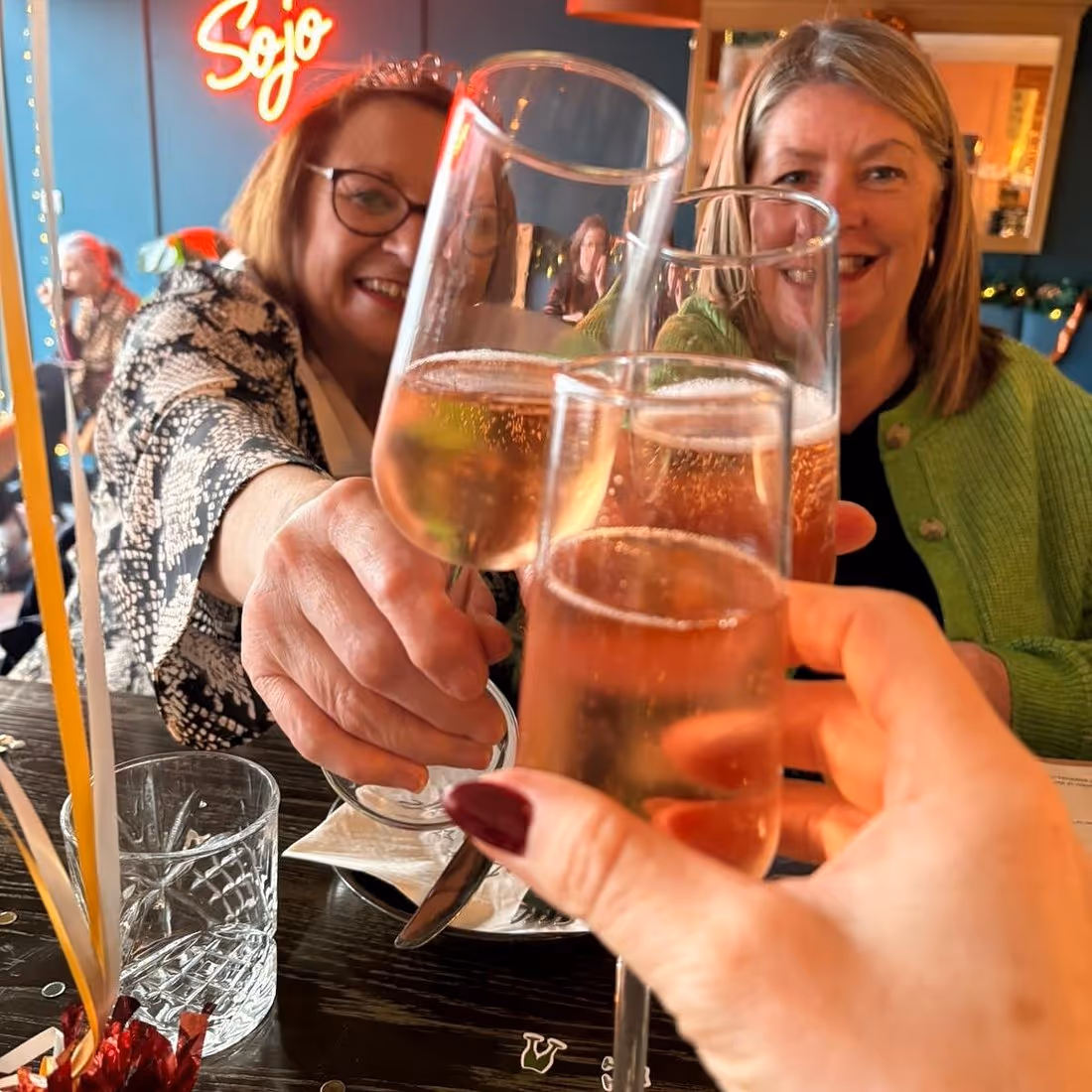 Three women clinking glasses of sparkling wine in a cheerful toast at a restaurant.
