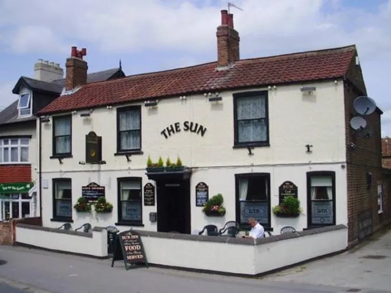 Exterior of a two-story pub named 'The Sun' with outdoor seating and white walls.
