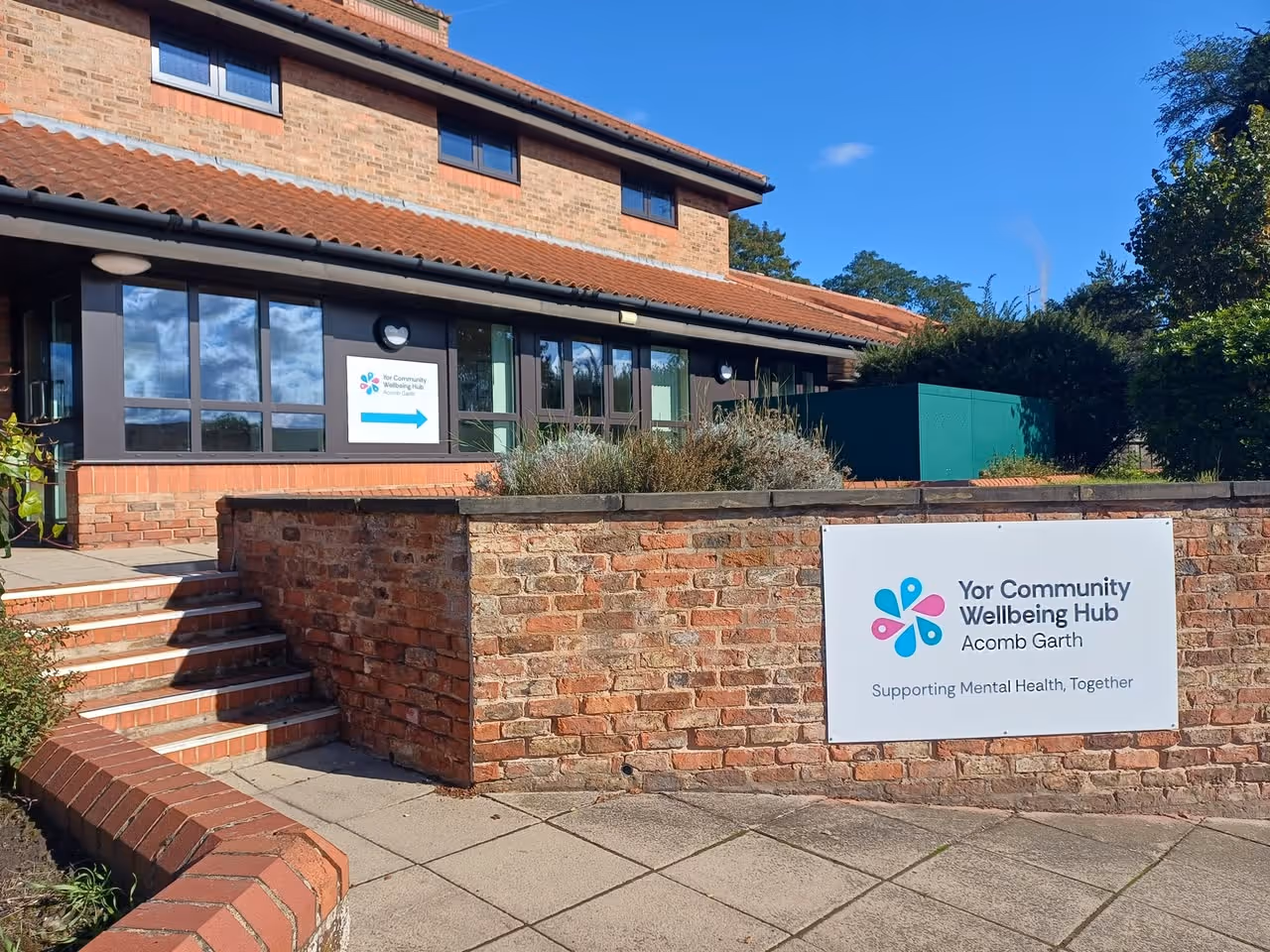 Brick building with signs for Yor Community Wellbeing Hub, Acomb Garth, supporting mental health.