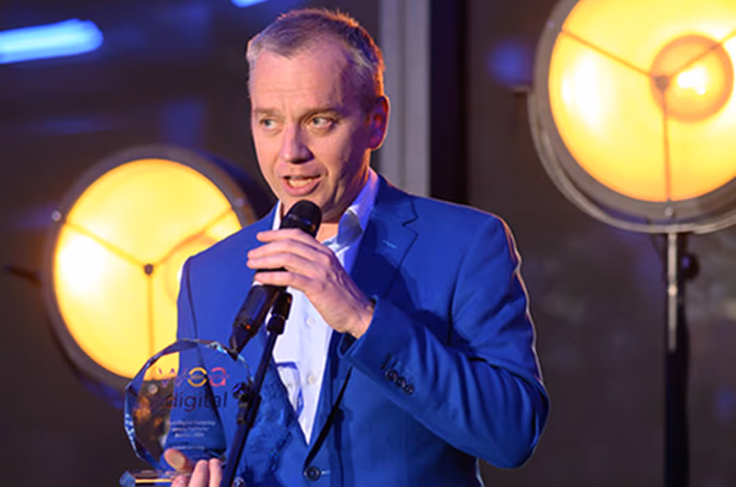 Bărbat în costum albastru ținând microfon și trofeu, la un eveniment Instant Factoring cu lumini mari.