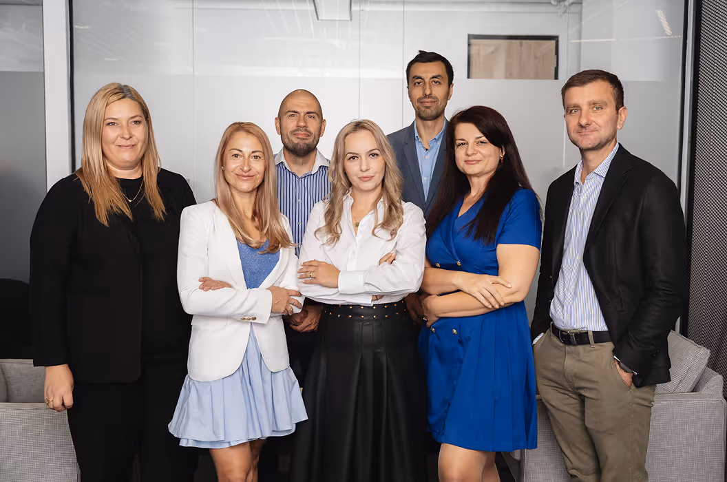 Șapte colegi din echipa de factoring stau împreună la birou și zâmbesc spre cameră.