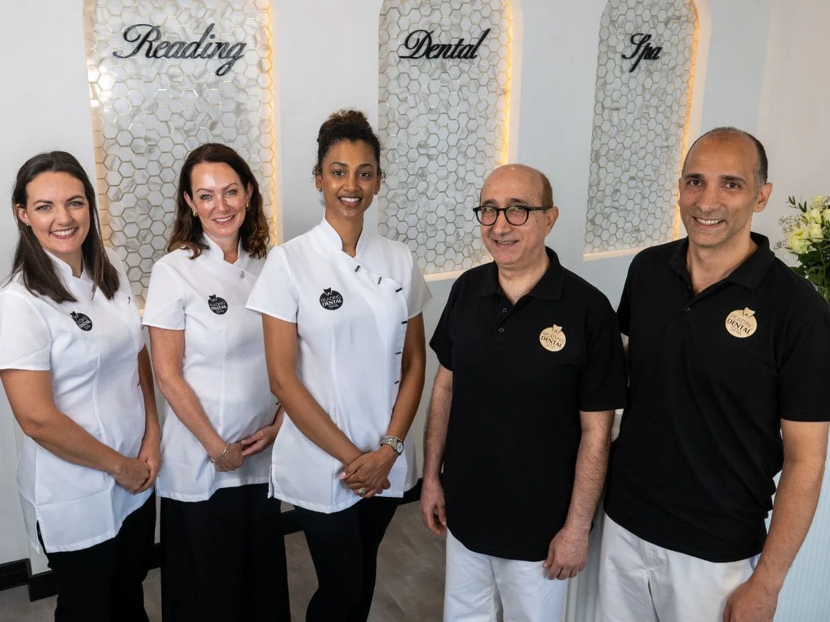 Group of three female and two male dental and spa staff posing and smiling indoors.