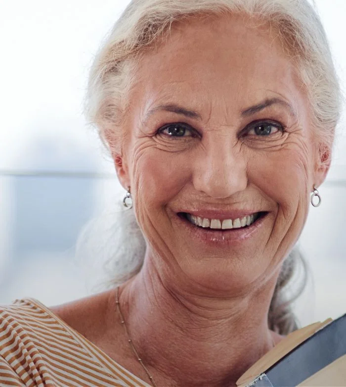 Smiling elderly woman with gray hair and striped top holding a book.