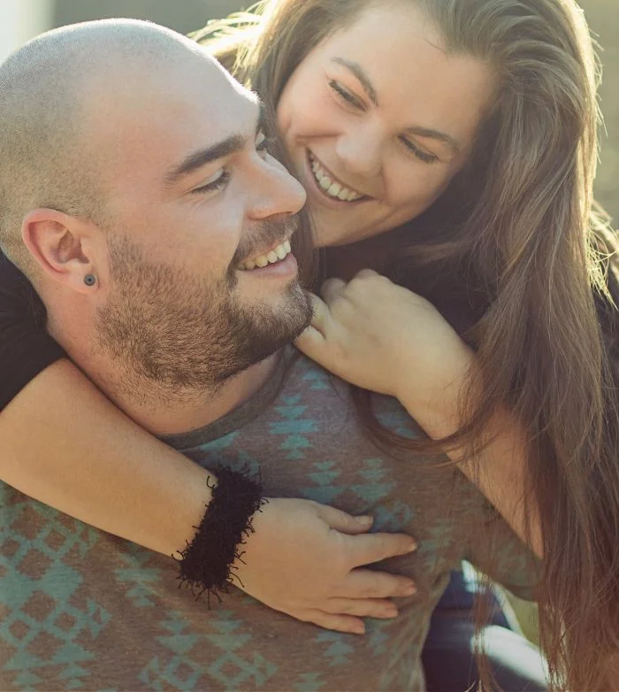 Smiling woman with long hair embraces a smiling bald man wearing a patterned shirt.