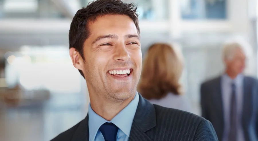 Smiling young man in a suit with two blurred people in the background.
