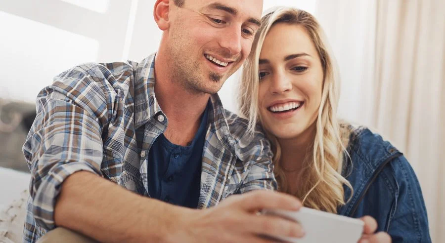 Smiling man and woman looking together at a smartphone screen.