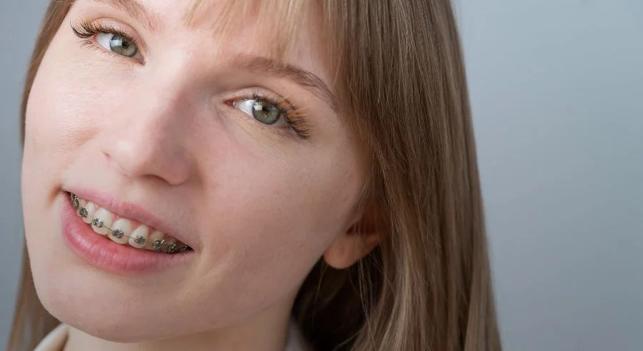 Close-up of a smiling woman with light brown hair and metal braces on her teeth.