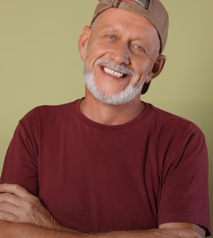 Smiling older man with a white beard wearing a backward cap and maroon shirt against a green background.
