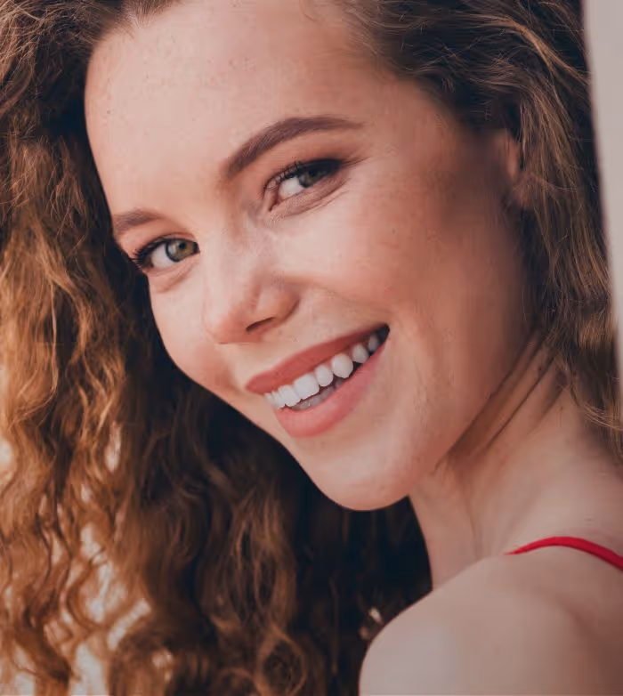Close-up of a smiling woman with curly hair and bright eyes wearing a red strap top.