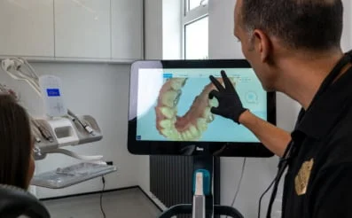 Dental professional showing 3D dental scan on a screen to a patient in a clinic.