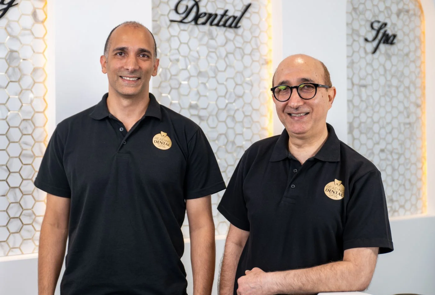 Two men wearing black Reading Dental Spa polo shirts standing and smiling indoors.