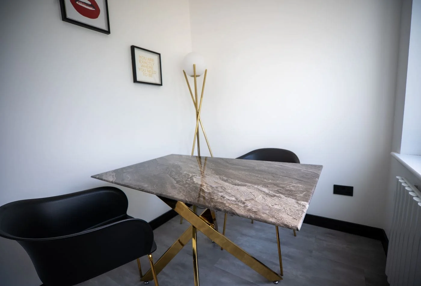 Modern dining area with marble table, gold legs, black chairs, floor lamp, and framed wall art.