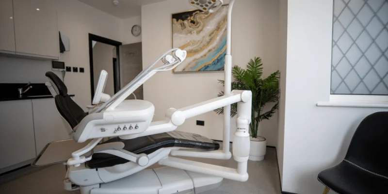 Modern dental chair with equipment in a clean, bright dental office room with a plant and artwork.