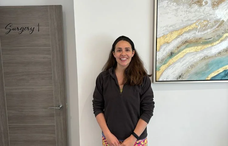 Smiling woman with dark hair standing in front of a door labeled Surgery 1 and abstract wall art.