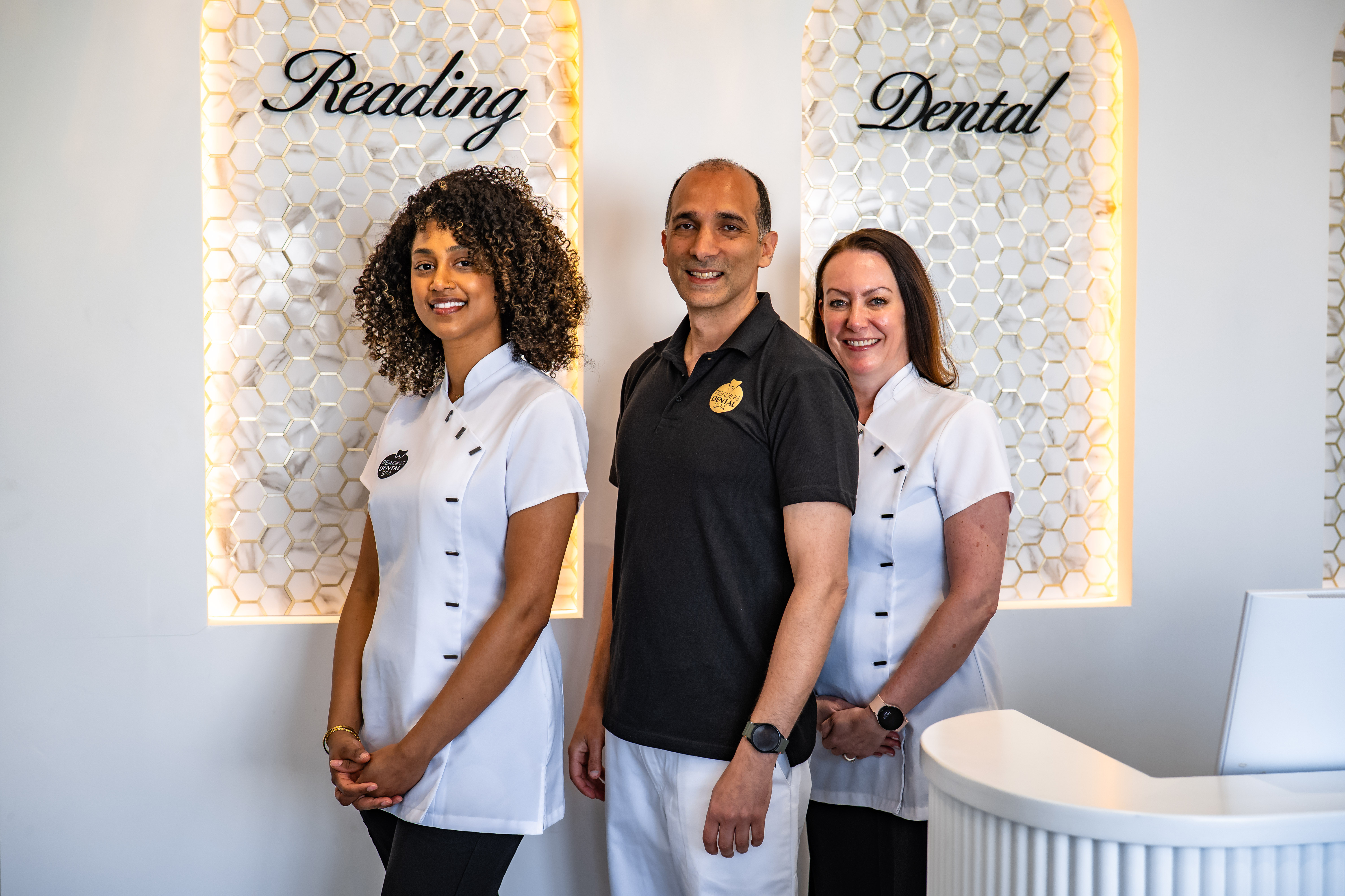 Three dental professionals smiling inside a modern clinic with Reading Dental signage behind them.