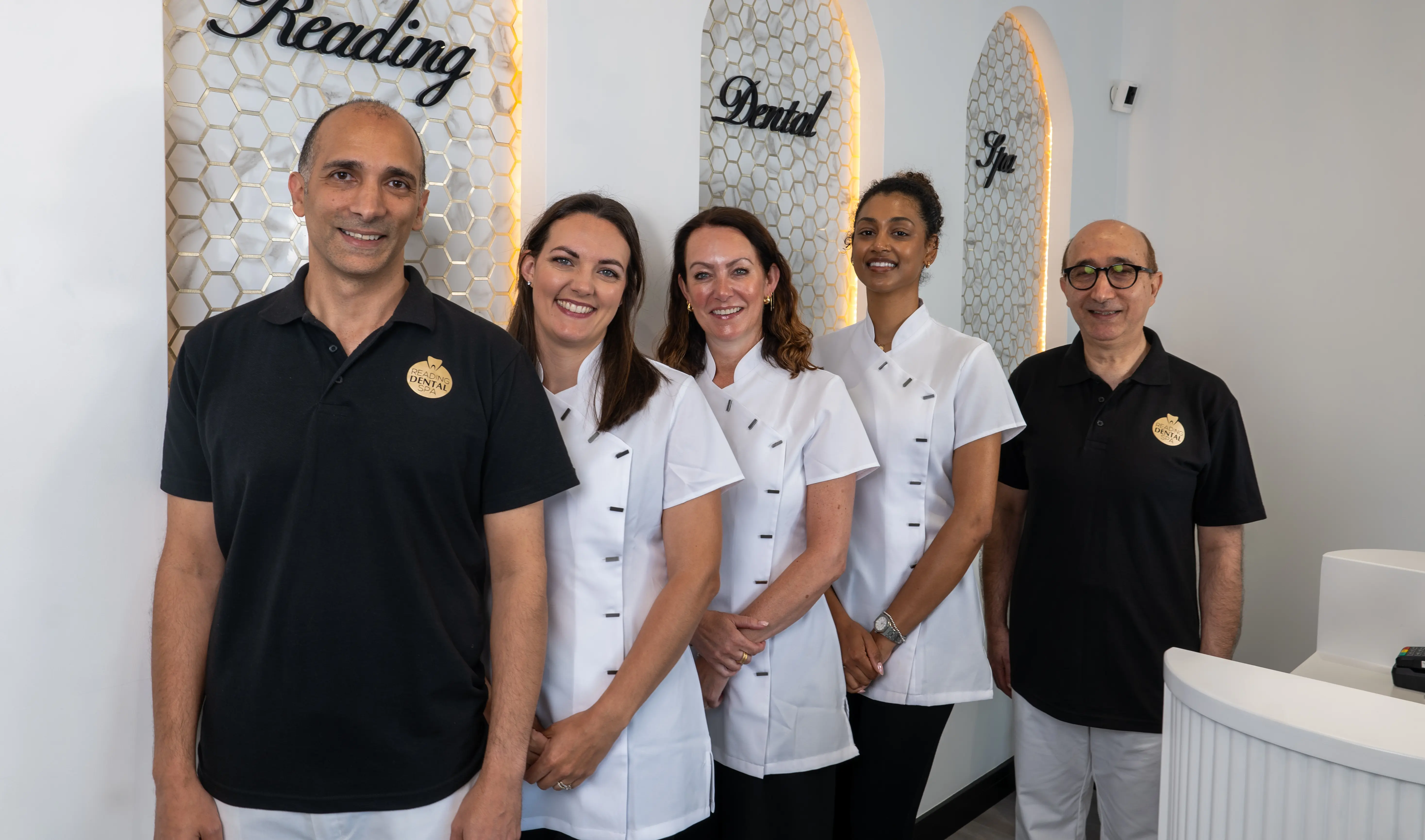 Five dental staff members in uniform smiling inside a dental spa with honeycomb wall panels.