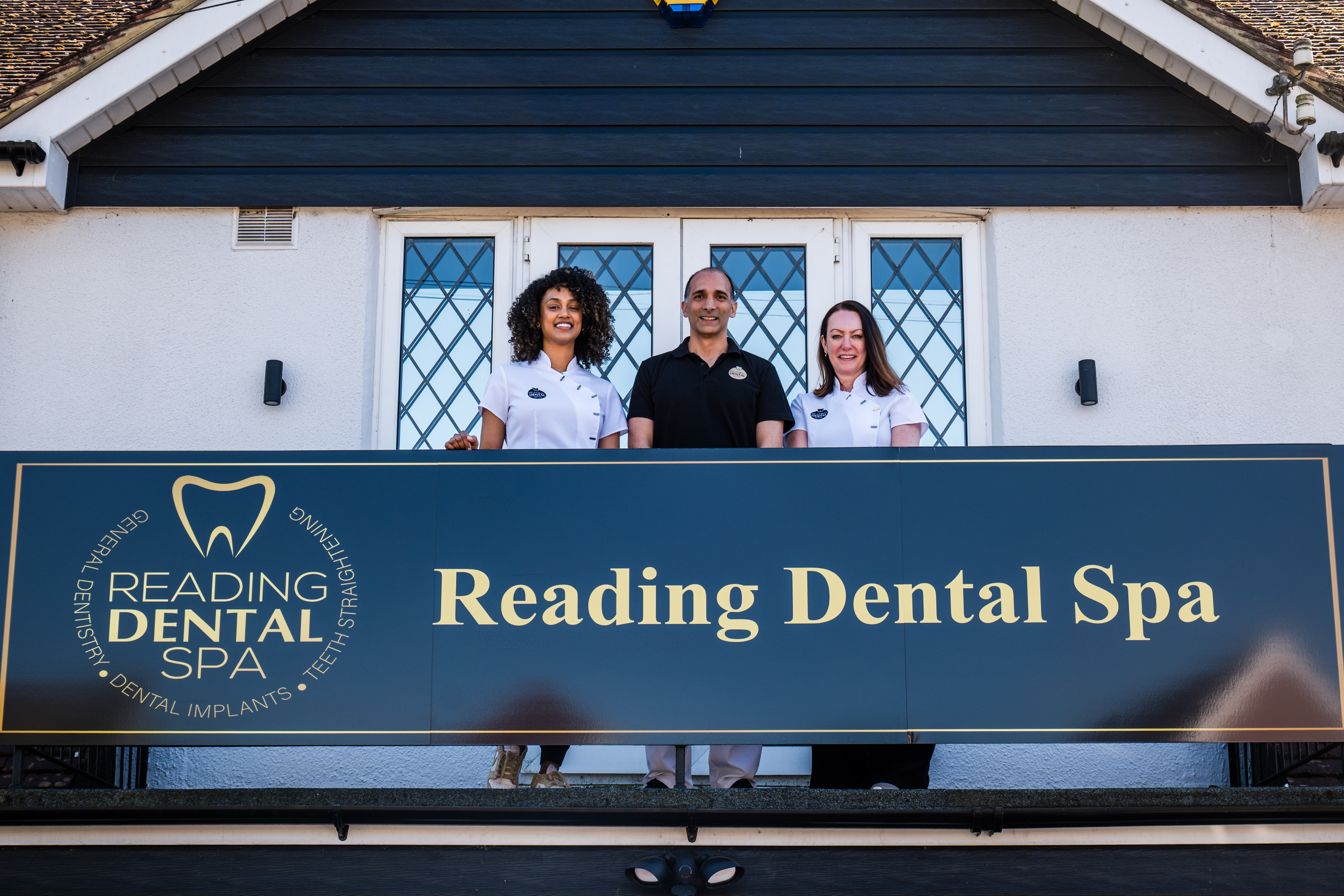 Three dental staff standing behind a Reading Dental Spa sign on a balcony in front of a building.