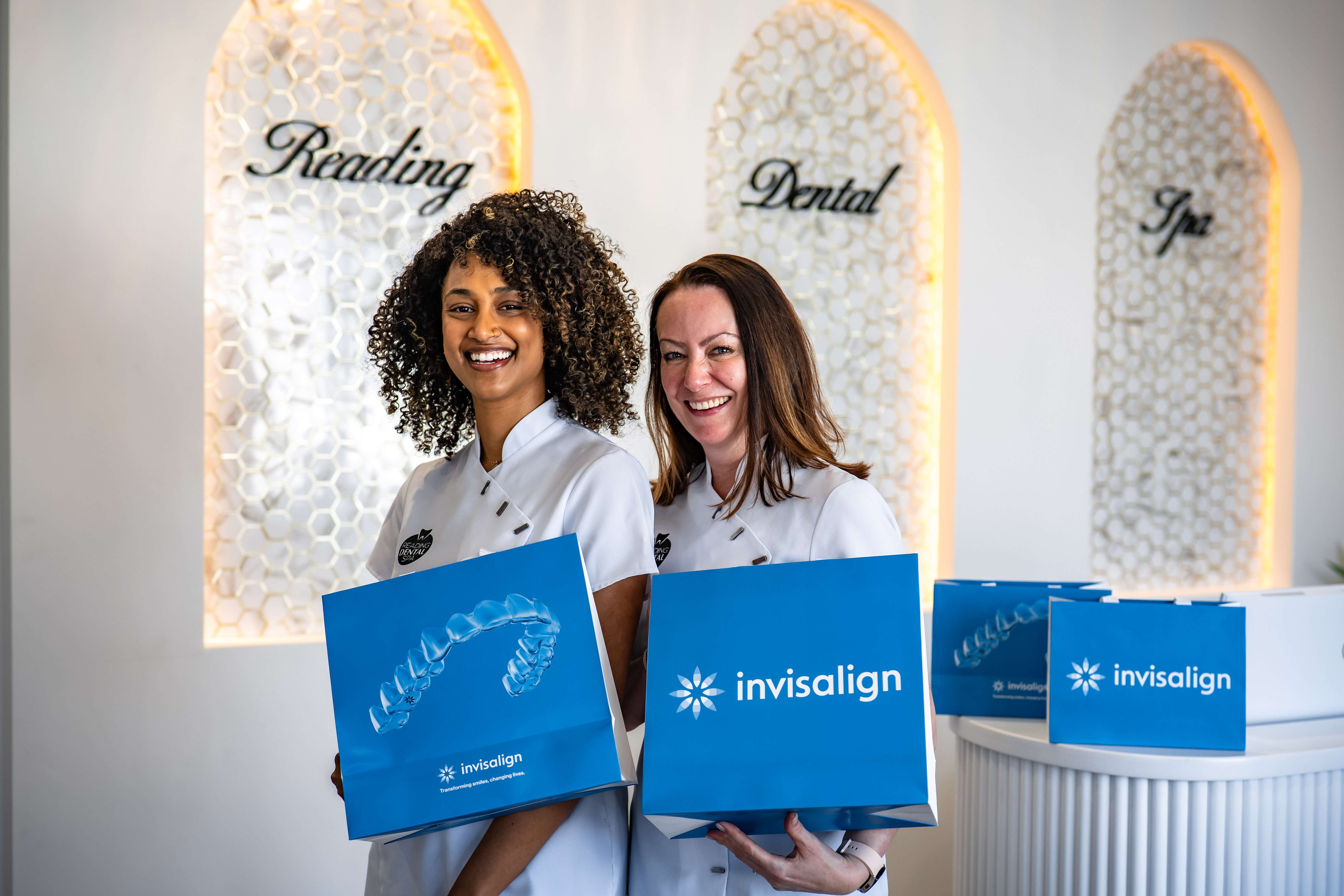 Two dental professionals smiling and holding blue Invisalign bags at Reading Dental Spa.