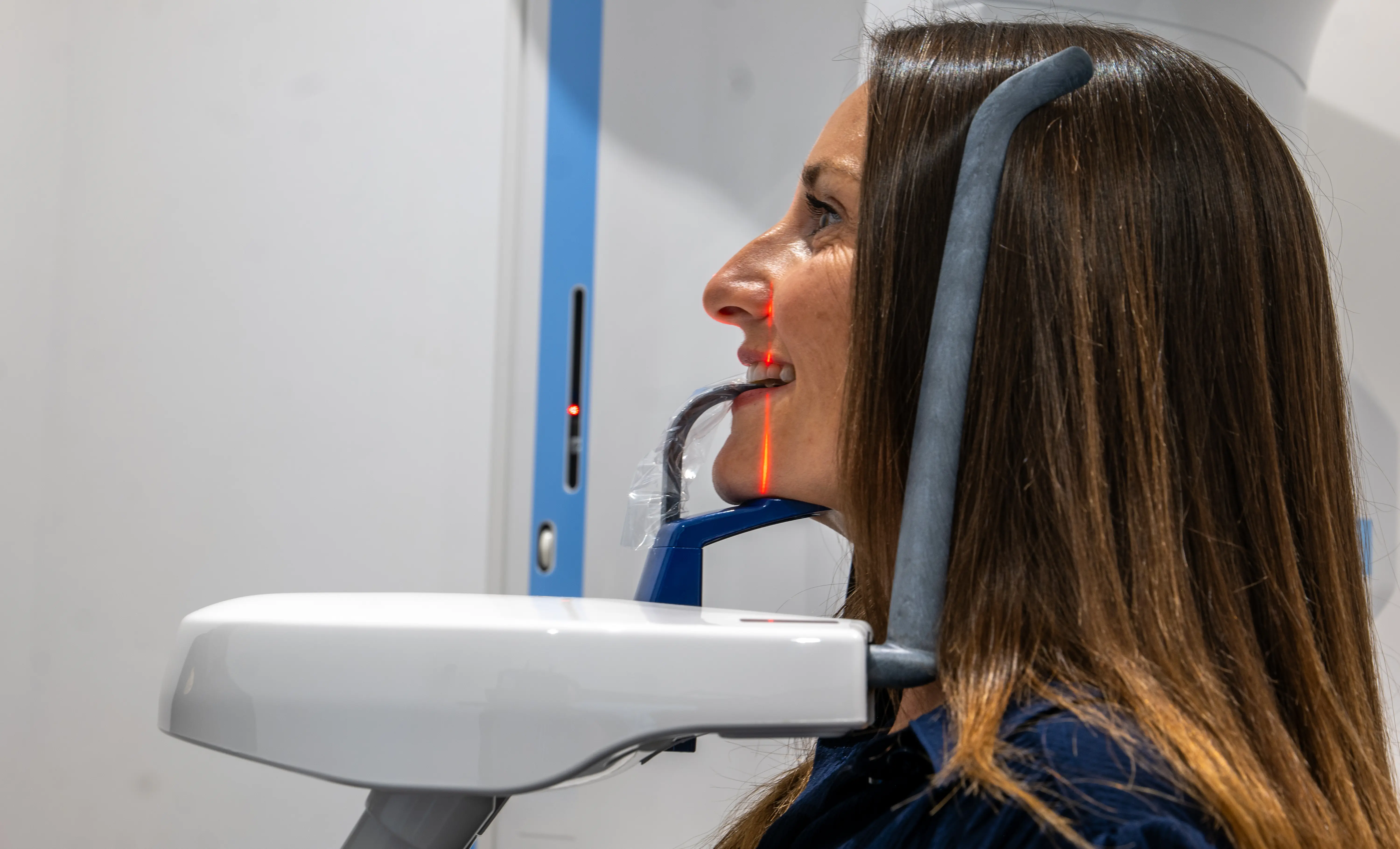 Side view of woman using a dental 3D scanner machine with red laser lines on her face.