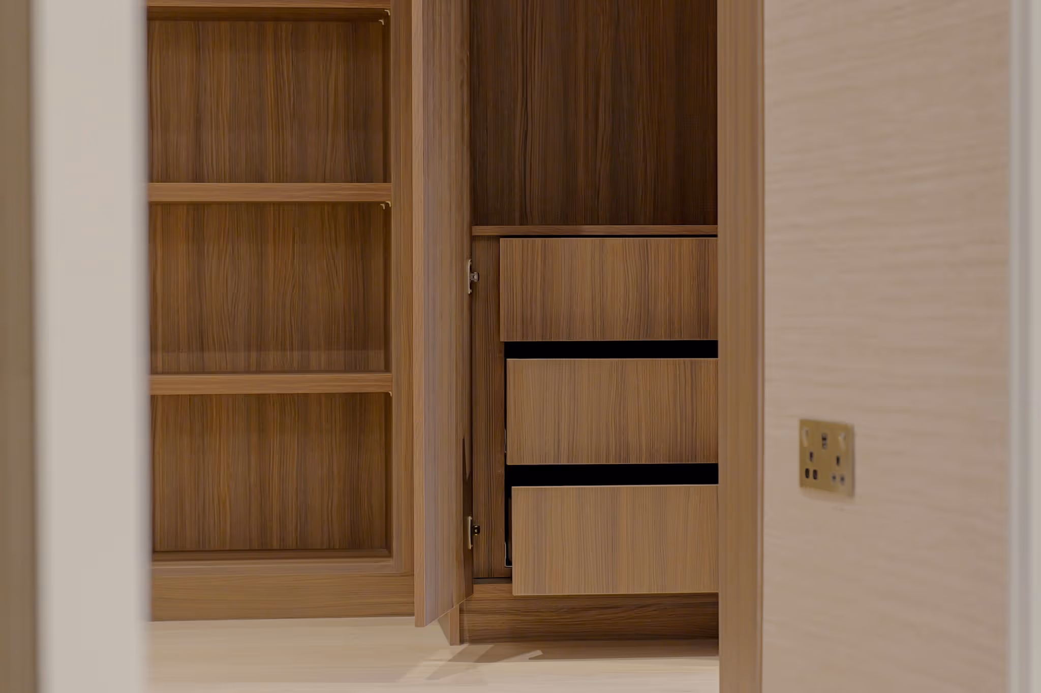 Open wooden cabinet with shelves and drawers inside a room with beige walls and floor.