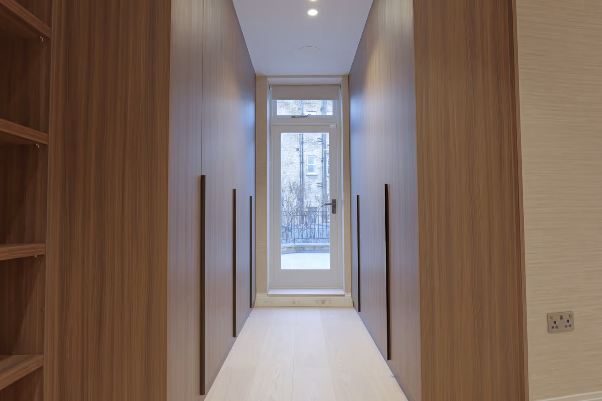 Narrow hallway with wooden closets on both sides and a glass door at the end.