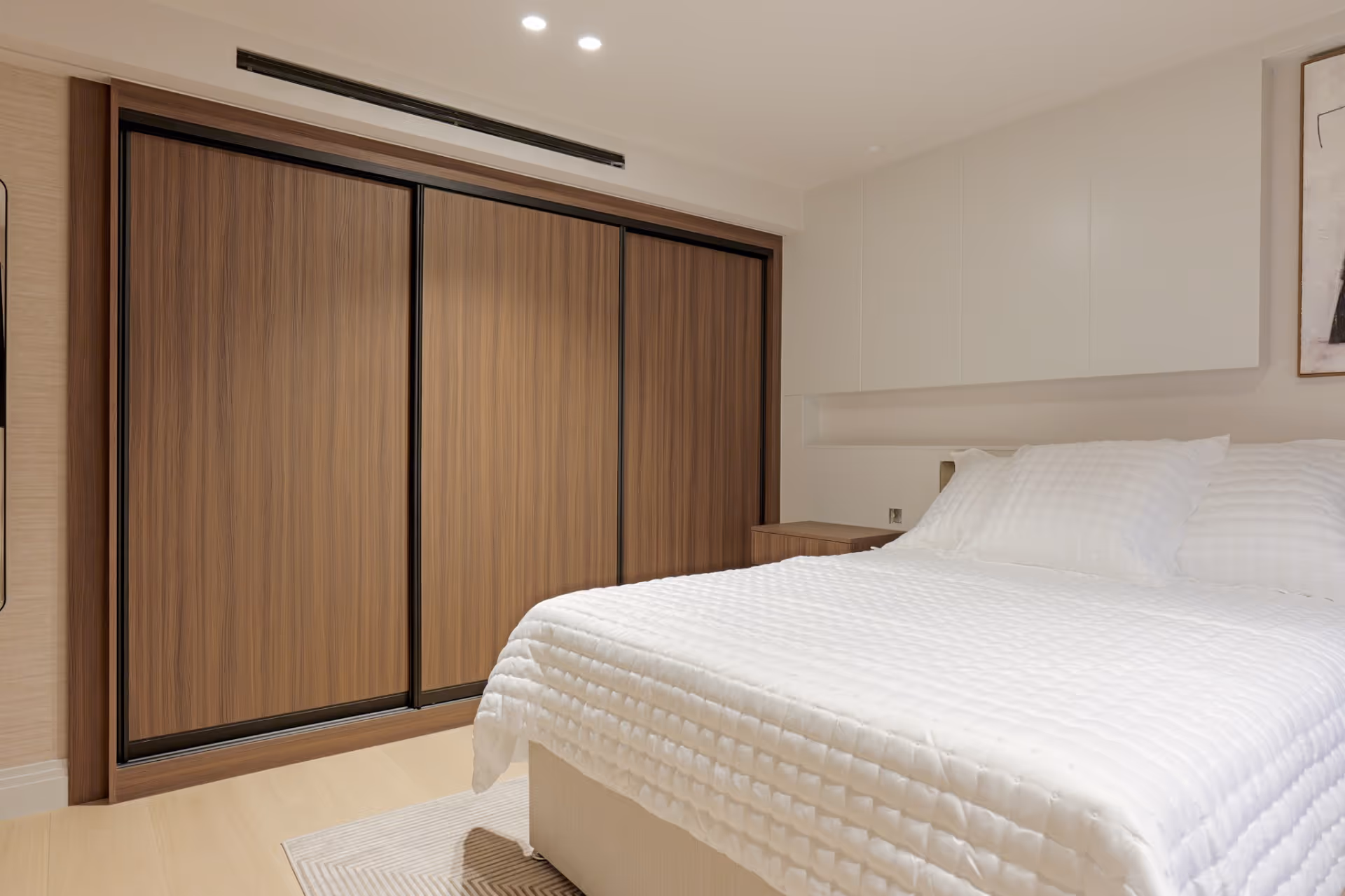 Modern bedroom with white bedspread, pillows, nightstand, and large wooden sliding door wardrobe.