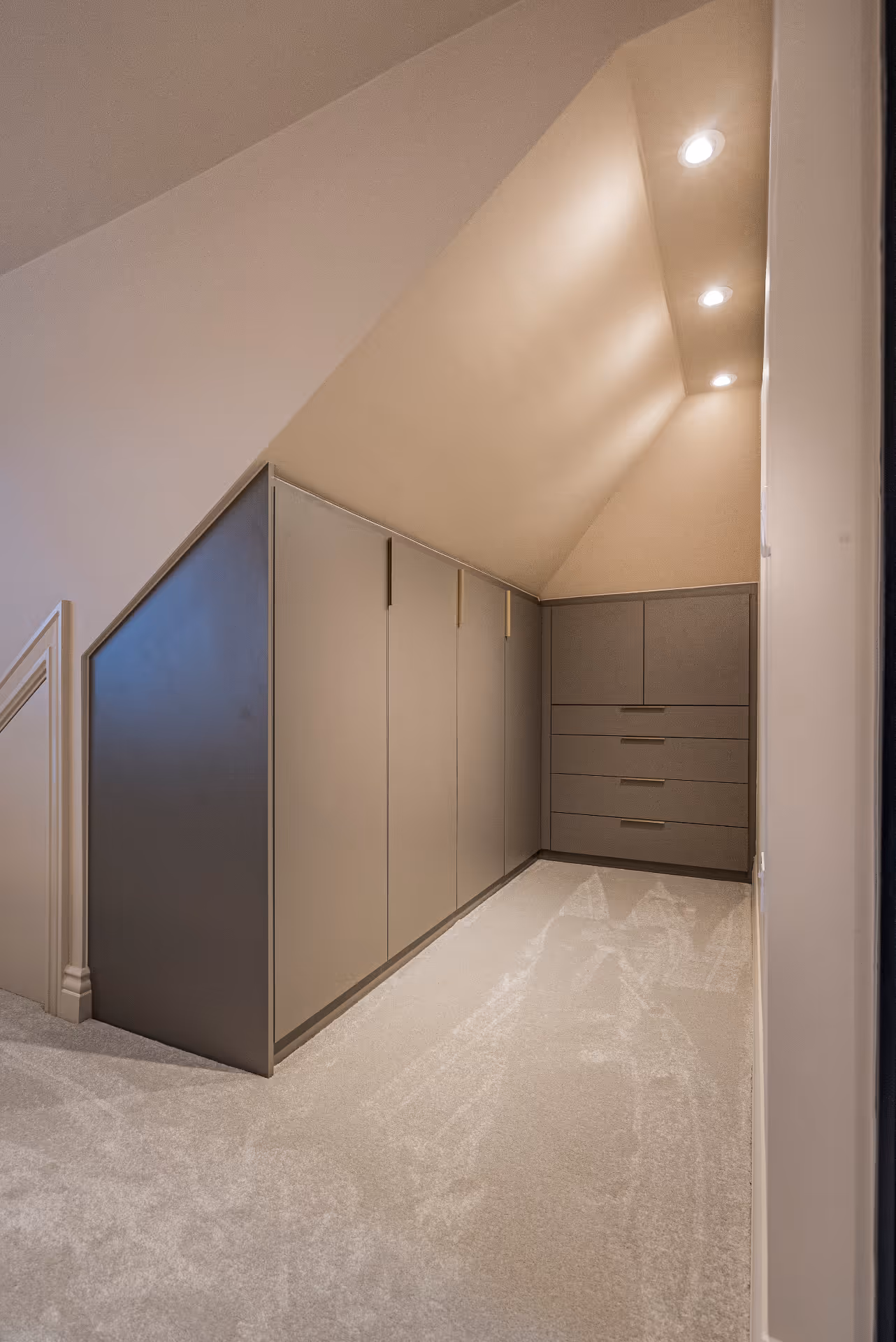 Loft wardrobe with angled ceiling, recessed lights, carpeted floor, and built-in gray cabinets and drawers.