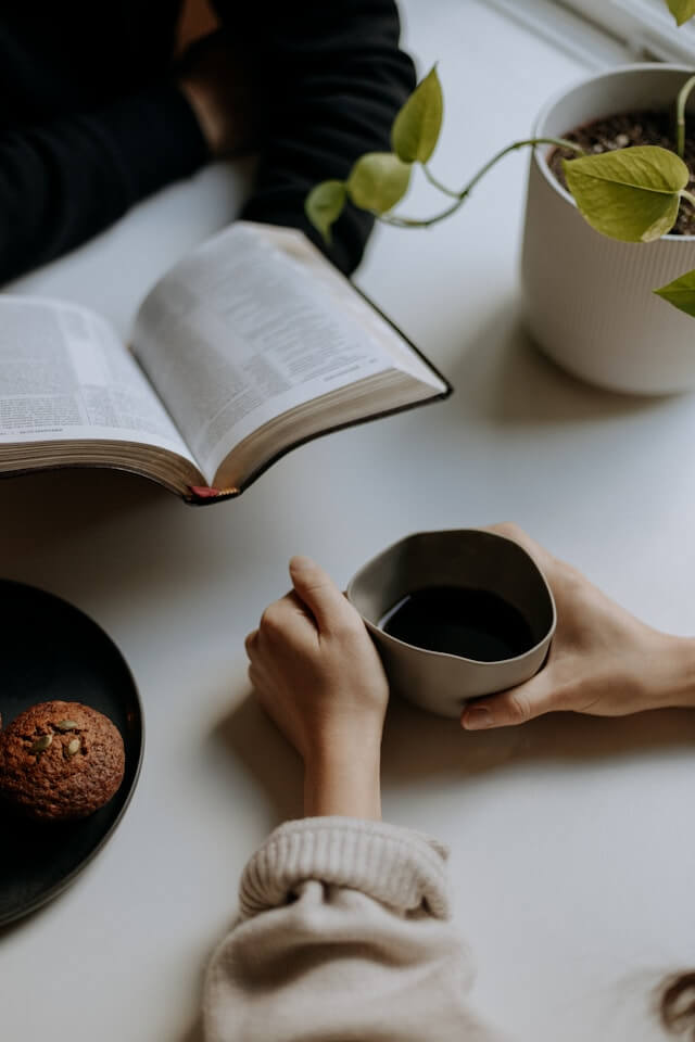 An overhead view of two people sharing a cup of coffee and reading an open book together, representing community study.