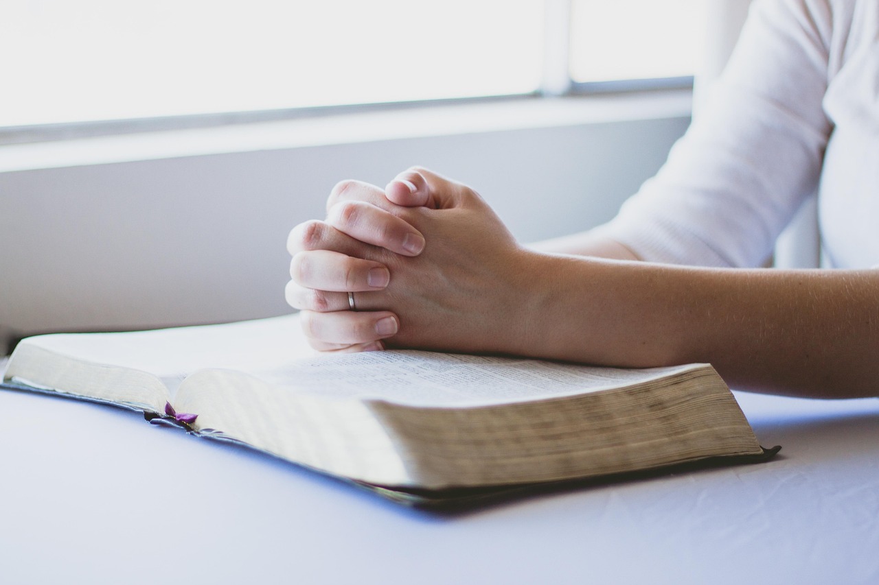 Hands resting on an open Bible while praying, focusing on divine truth.