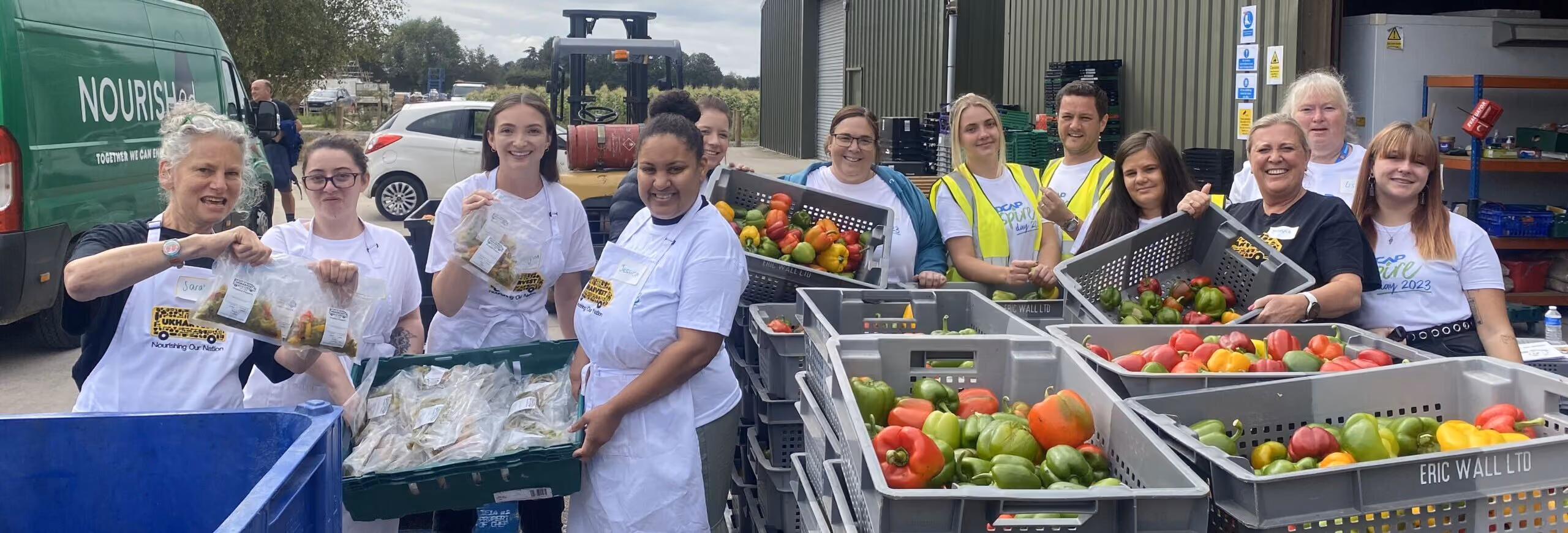 A group of volunteers wearing Fedcap Inspire T-shirts sort fresh produce into crates at a food distribution event.
